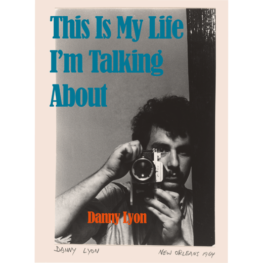 Book cover featuring the photo of a man pointing a camera at thte viewer and the title in blue characters positioned at the top left edge.