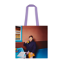 A tote back featuring an photograph of a man sitting at a dining table with fried eggs on his face behind his glasses.