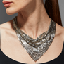 A white woman with blonde hair is wearing a chainmail silver necklace. The photo shows a close up of her neck, chin and shoulders..