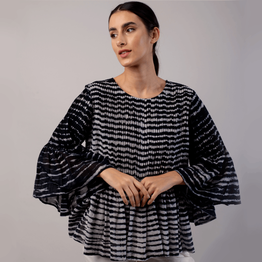 A model with dark hair wearing a black and white pleated blouse with fluted sleeves.