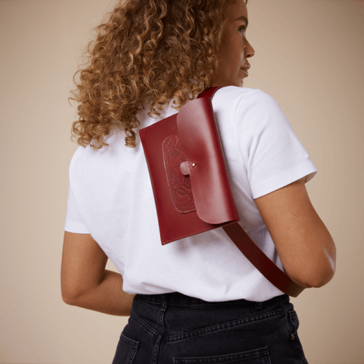 A woman showing her back to the camer, wearing a white t-shirt and a red crossbody leather bag.