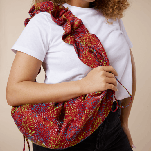 A woman wearing a white t-shirt and carrying a red stitched bag over her shoulder.