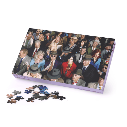 Jigsaw puzzle box featuring the photograph of a crowd of people. A few pieces of the puzzle are scattered next to the box.