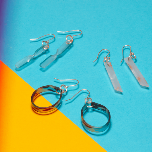 Three pairs of colourful hook earrings on a bright yellow and blue flat surface.