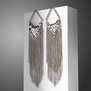 A pair of silver chainmail earrings hanging from a white block propped against a grey background.
