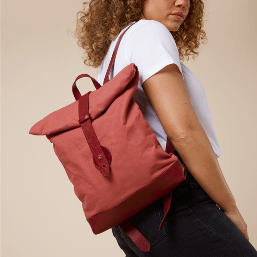 A woman wearing a white t-shirt and black jeans carrying a red backpack.