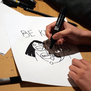 A kid draws with a black sharpie. The image shows a close up on the hands and paper.