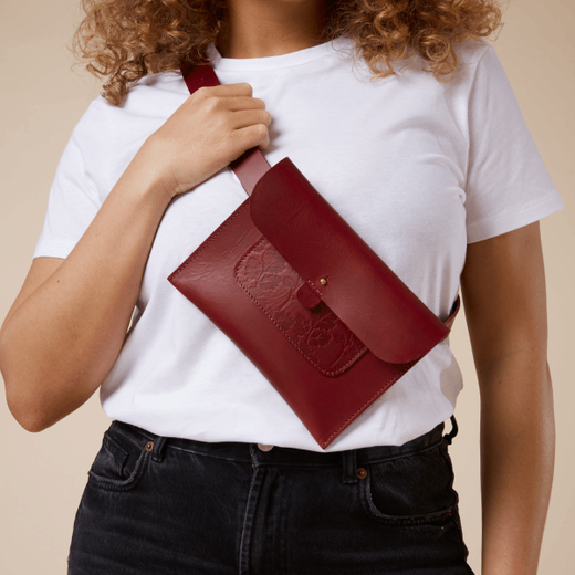 A woman with curly blonde hair wearing a white t-shirt and a red crossbody leather bag.