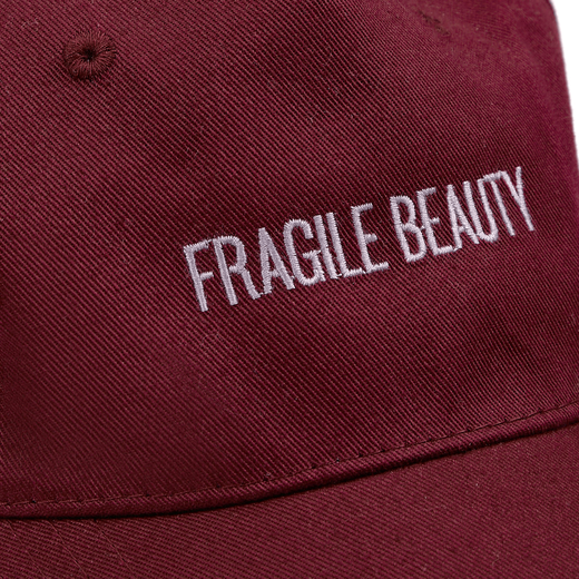 Embroidered purple text spelling 'Fragile Beauty' in capital letters on maroon fabric.