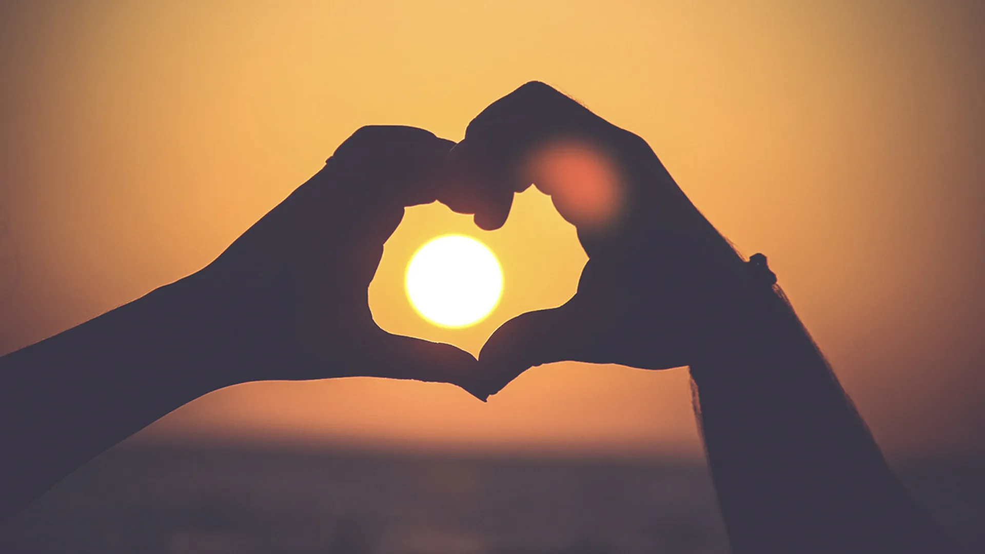 Silhouette of two peoples hands forming heart at sunset.