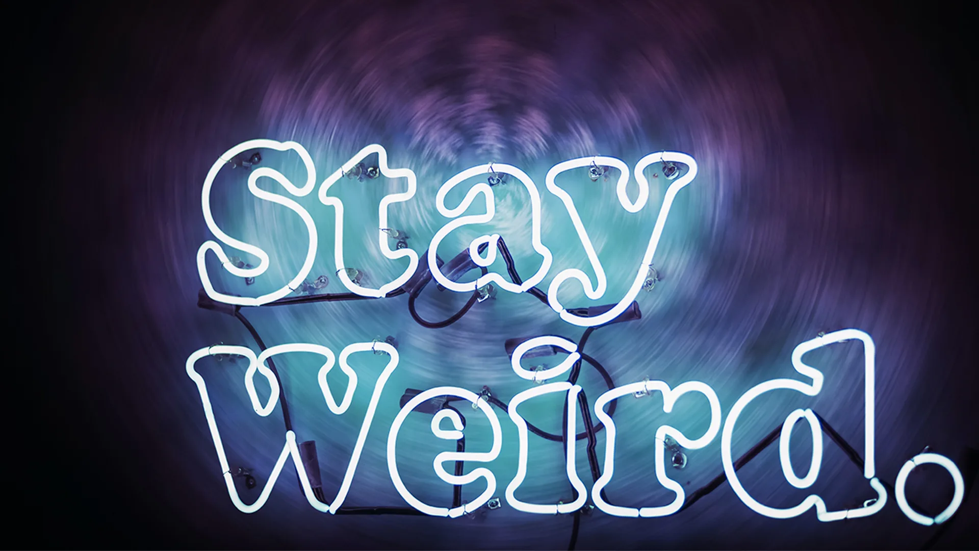 Neon 'Stay Weird' sign on a black wall.