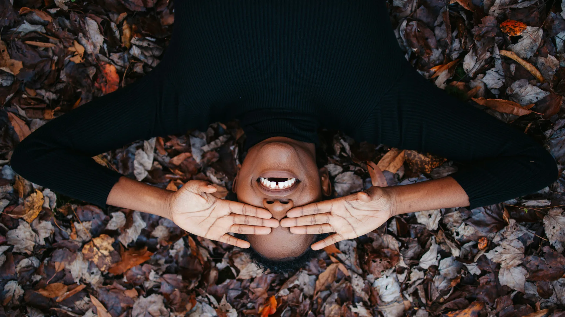 A woman lying on some leaves with her hands covering her eyes