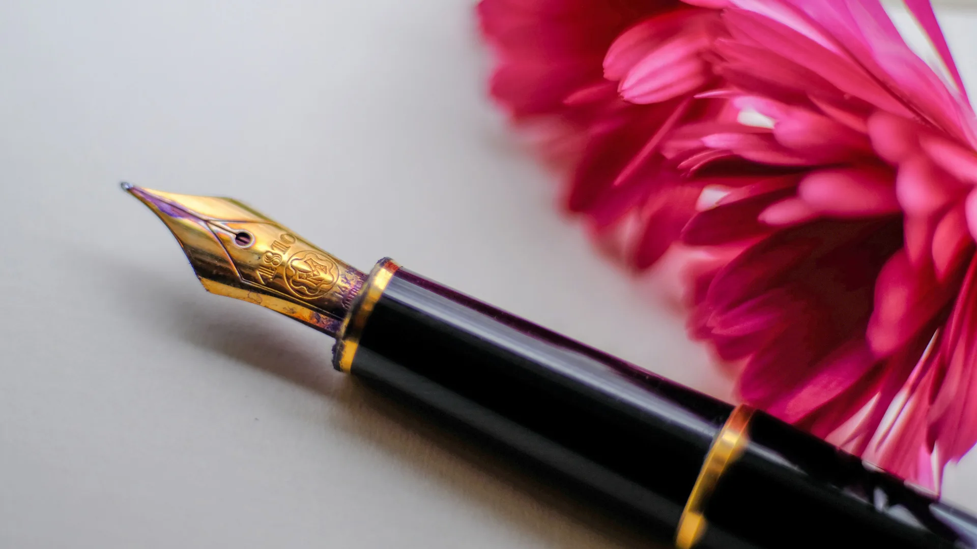 Photograph of a gold and black fountain pen next to pink flowers