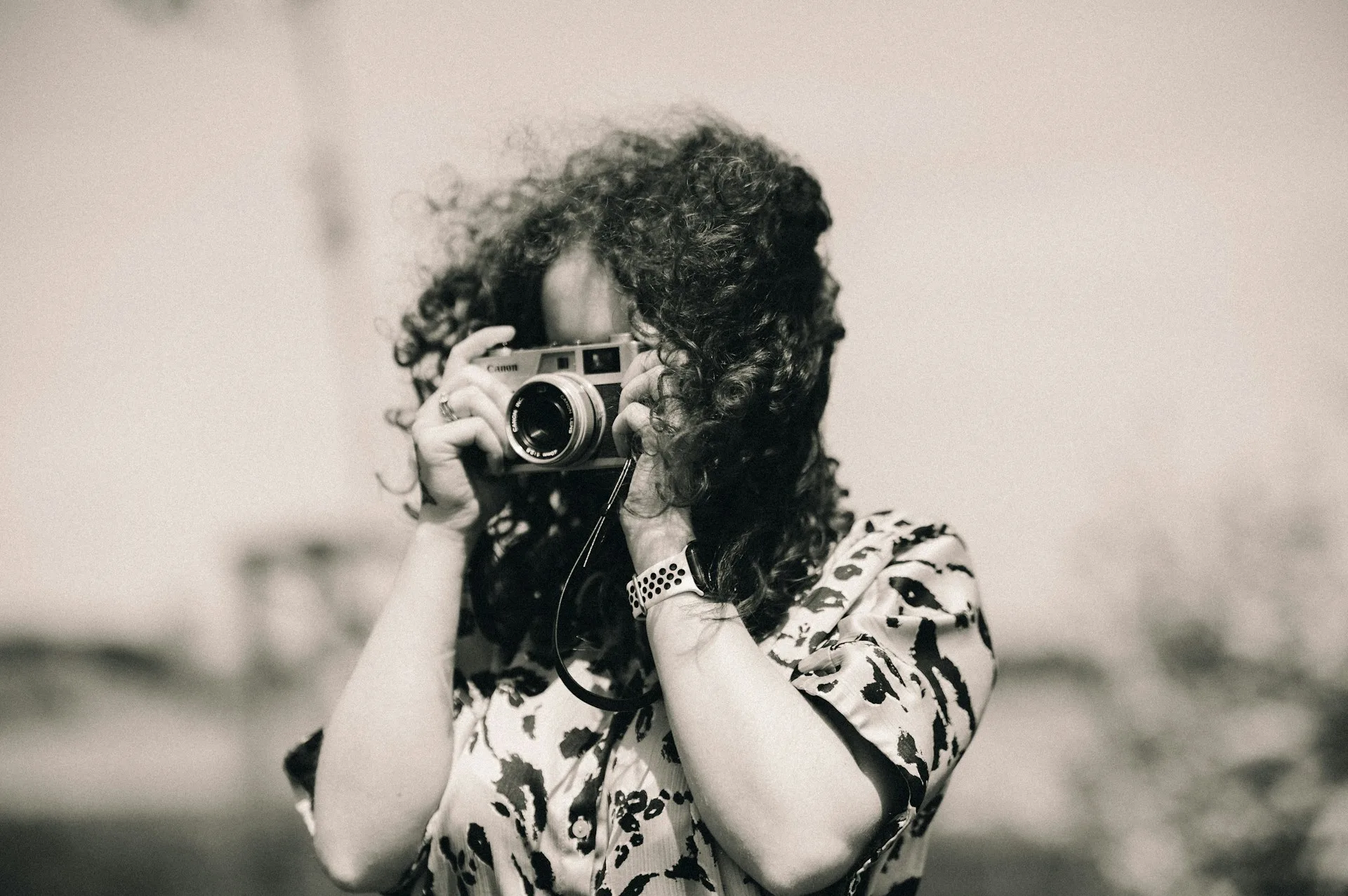 Sepia image of a woman taking a photo with a film camera