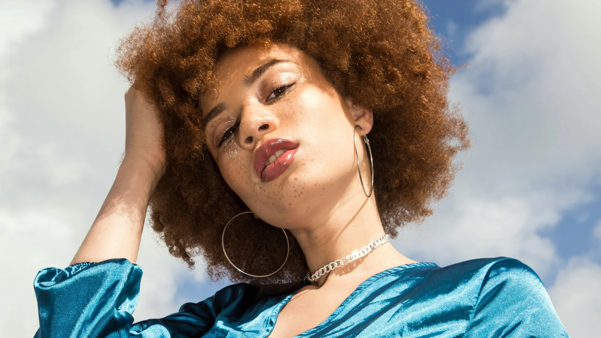 Ginger haired woman posing looking at the camera wearing a blue satin dress with sky behind her