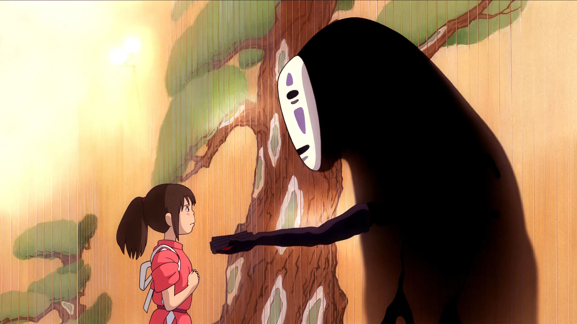 A still from the animated film Spirited Away showing the character No Face giving something to Chihiro against a bath house background