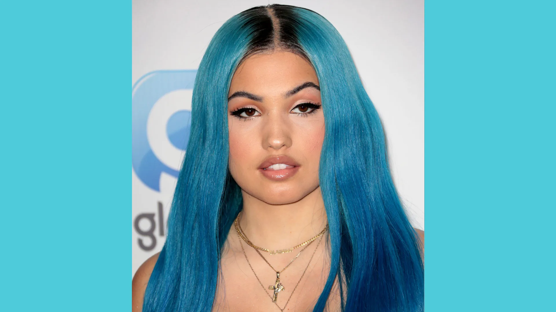 A photograph of the singer Mabel looking face on to the camera with blue hair and necklaces.