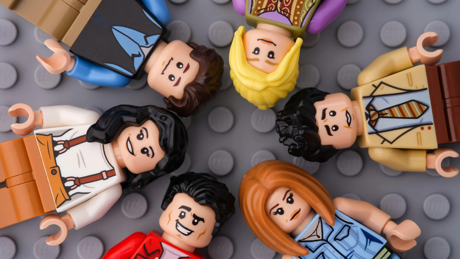 A photograph of the cast of Friends as LEGO minifigures lying in a circle head to head on a grey LEGO floor