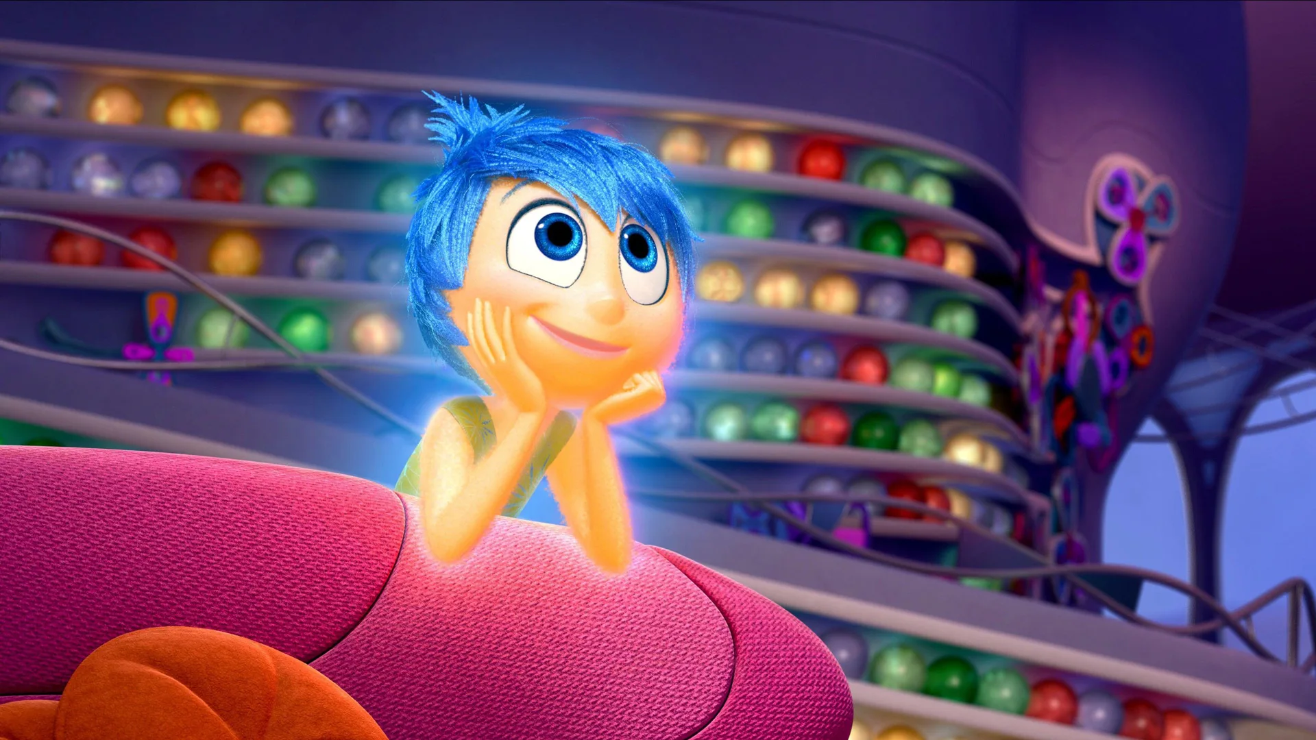 A scene from Inside Out showing Joy smiling with her head in her hands leaning on a pink sofa against a background of memory balls on shelves