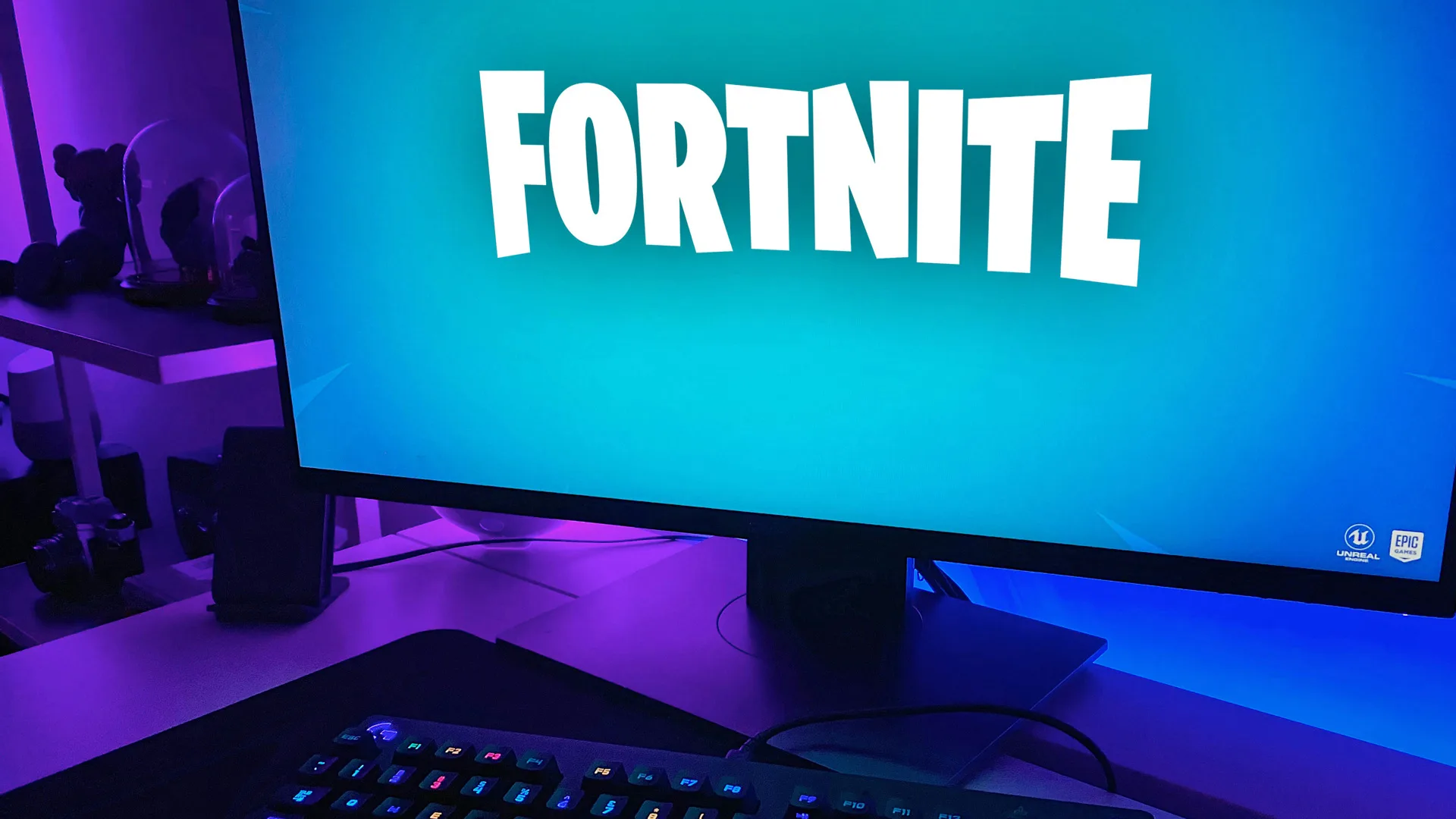 A photograph of a monitor saying the words FORTNITE with a blue background and a keyboard is just in shot