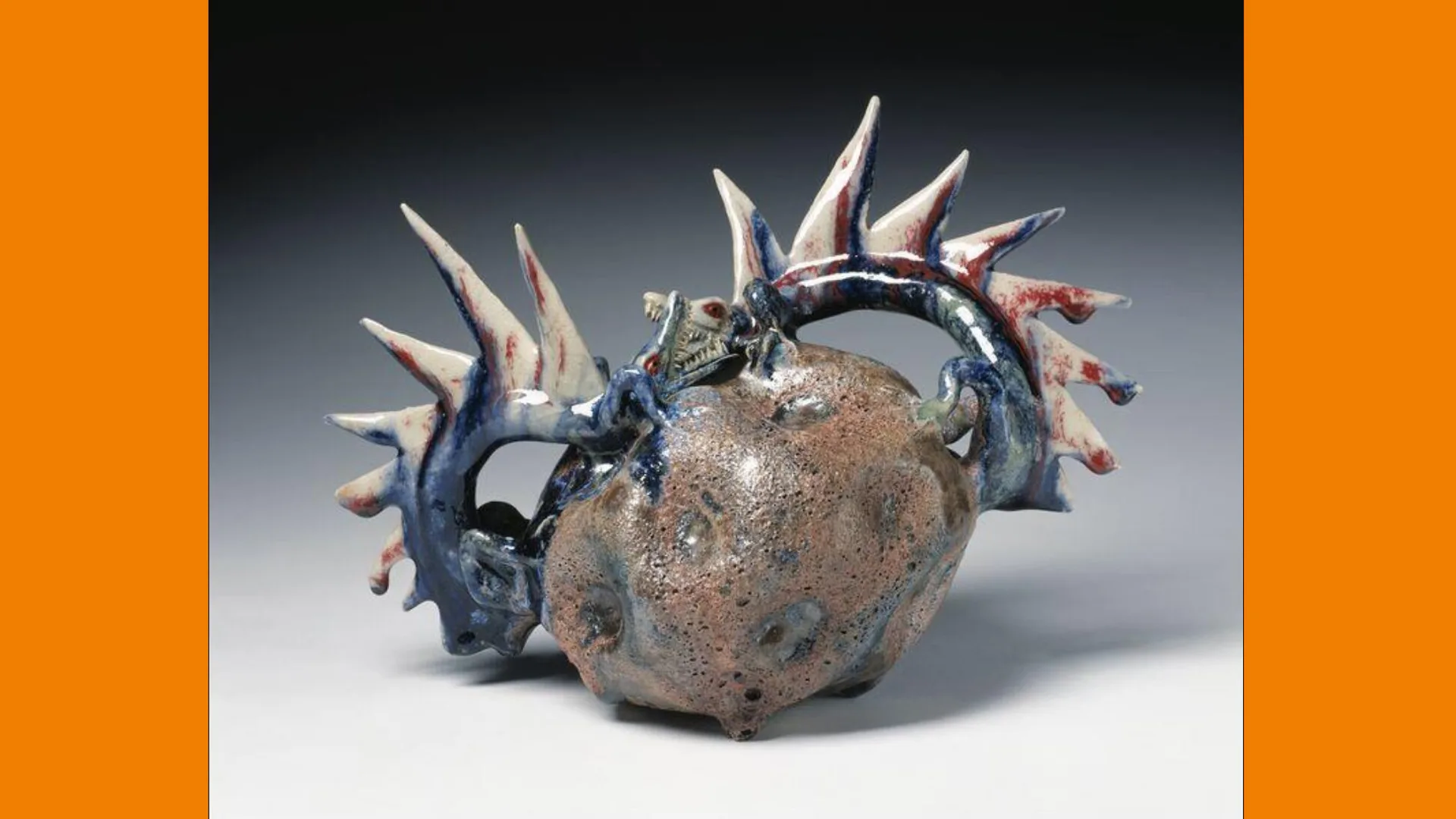 A photo of a scary looking sculpture with spiky horns and little teeth. It's supposed to be a dragon but could be anything. It is called Anger and sat against a grey background with orange borders.