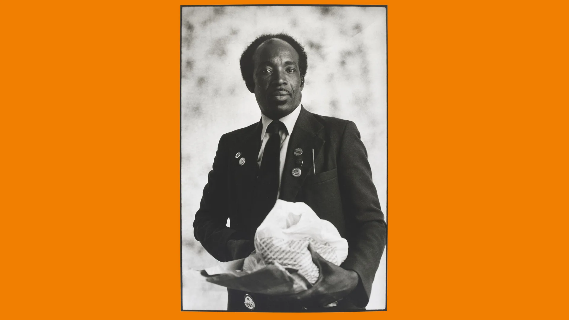 A photograph of a man holding a bag of food wearing a busman's uniform against a grey background with orange borders