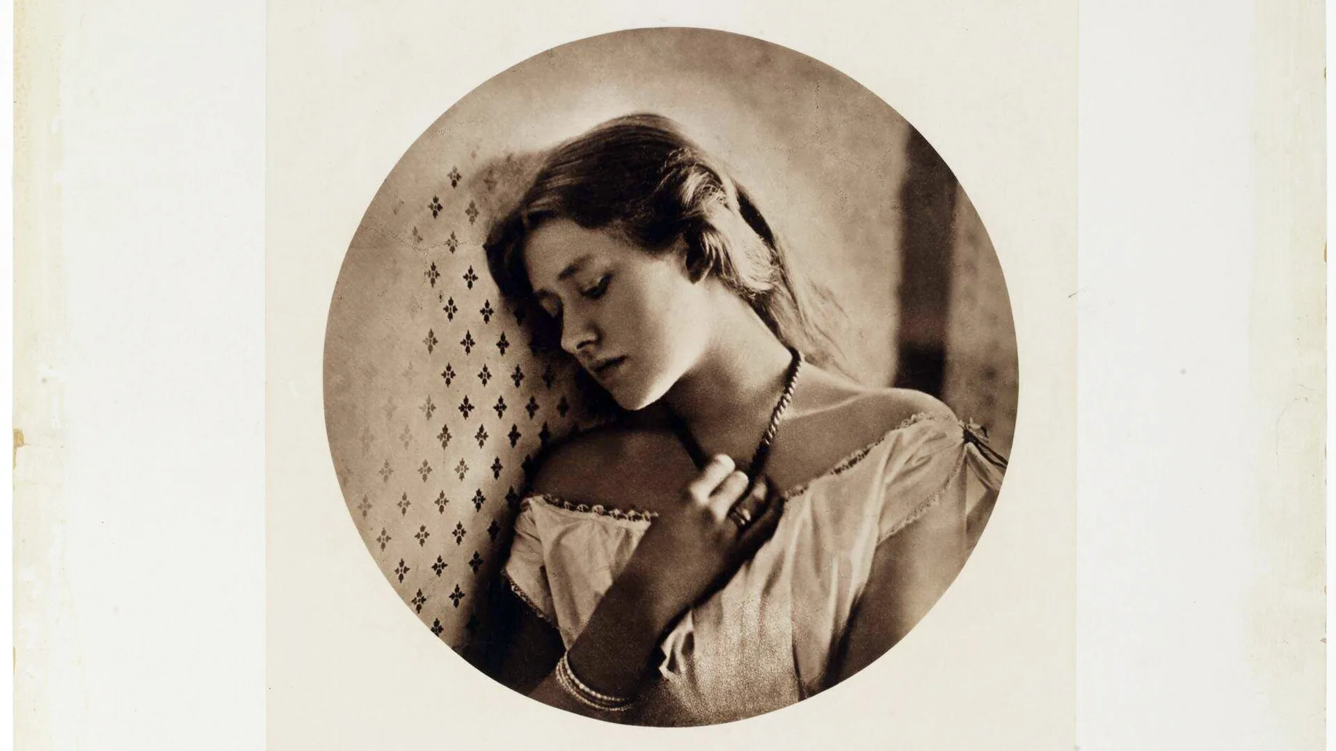 A photograph of a young woman in a white top looking sad and down holding her necklace. The photo is in sepia and a circle crop with grey borders.