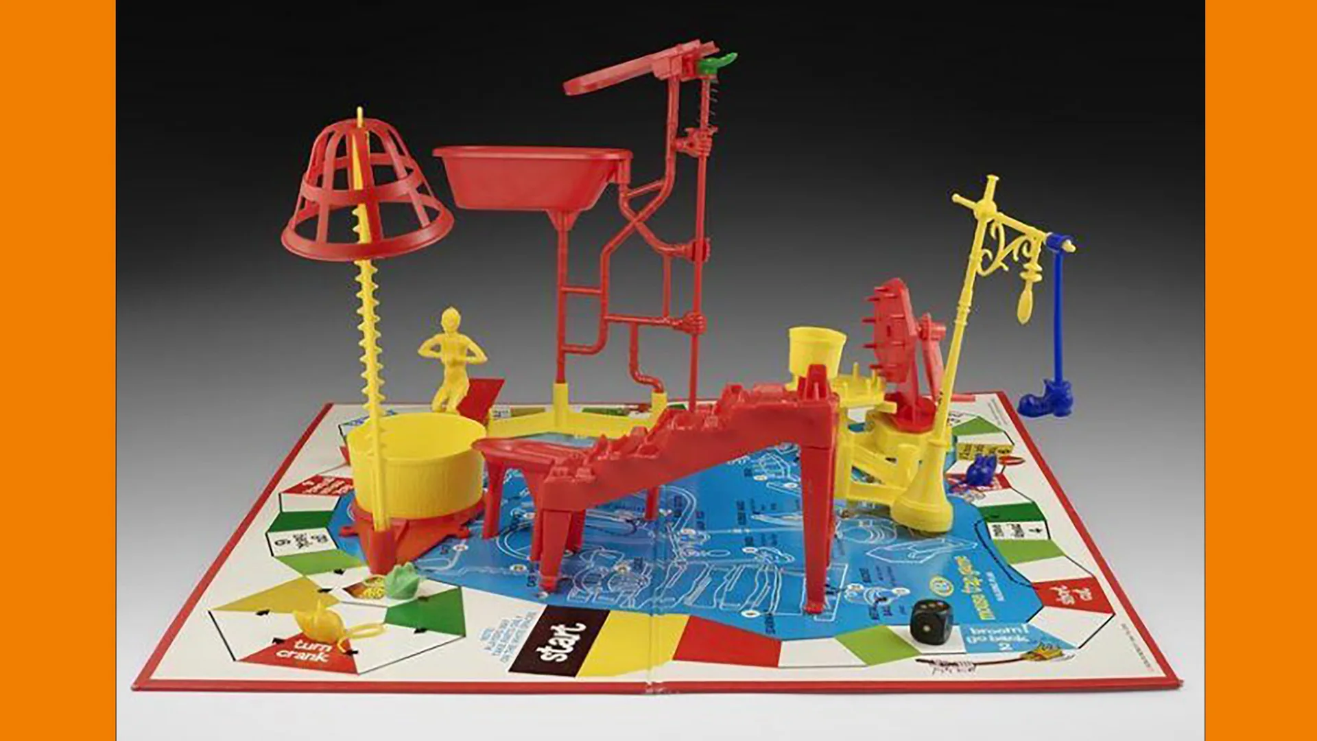 A photograph of the original 1960s children's game Mouse Trap which features colourful plastic pieces to make a moving contraption, on top of a board game to move your pieces. The game is against a grey background with orange borders.