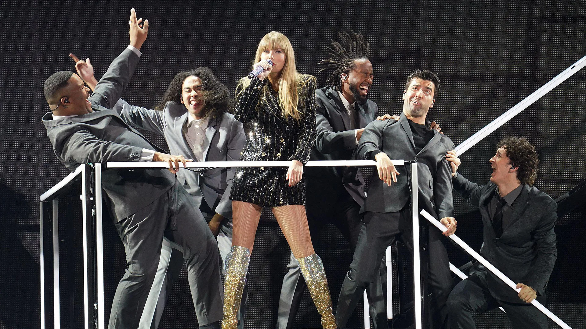 Taylor Swift and 5 male dancers wearing black suits perform on stage