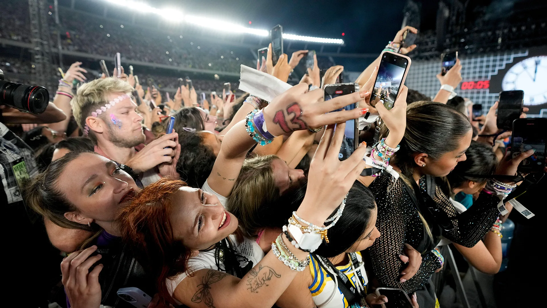 Group of fans at the Eras Tour concert in Argentina trying to take photos of the stage. Fan in foreground has the number 13 on hand