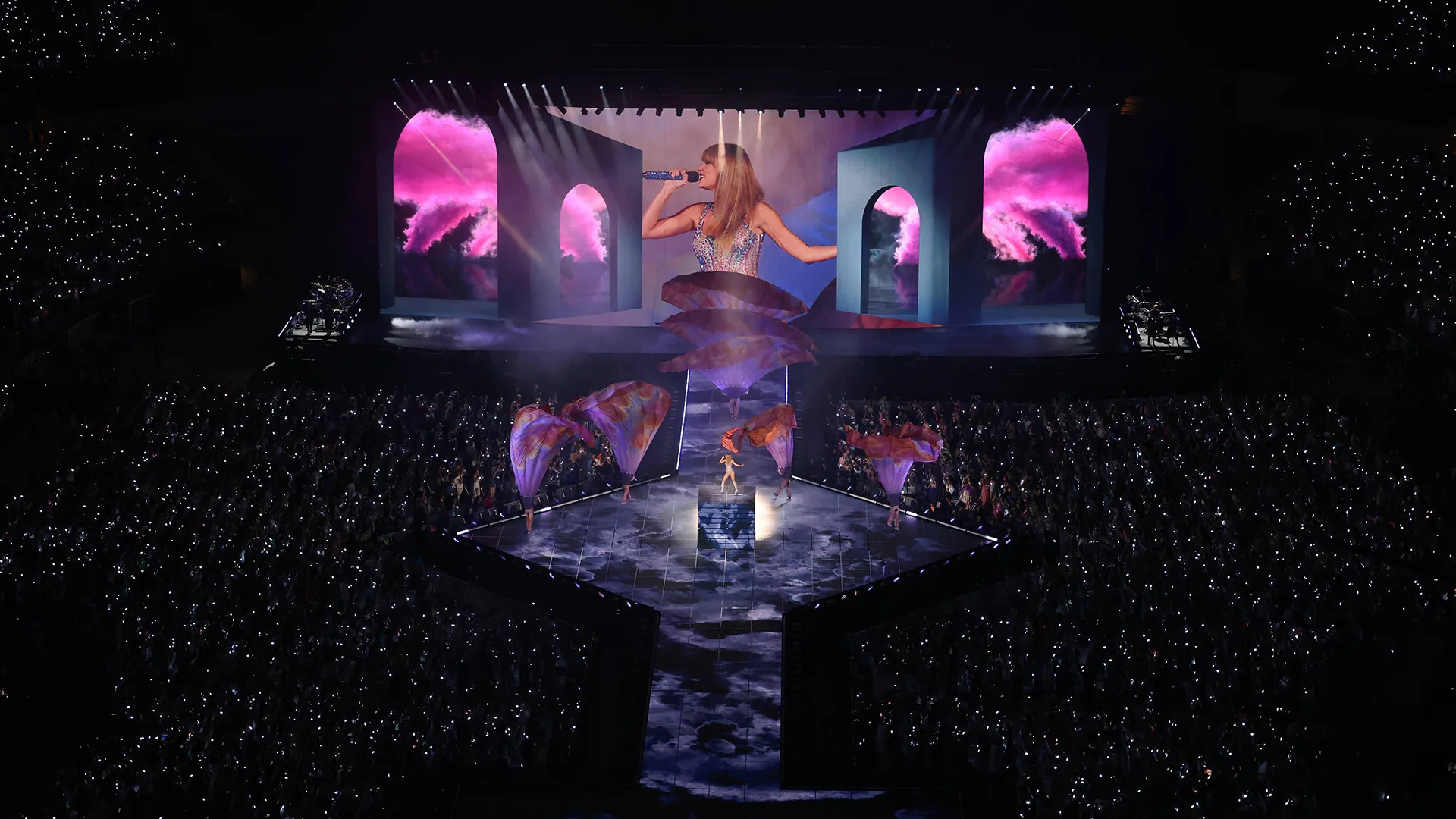 Wide landscape image of the Taylor Swift Eras tour stage, showing crowd and Taylor on stage