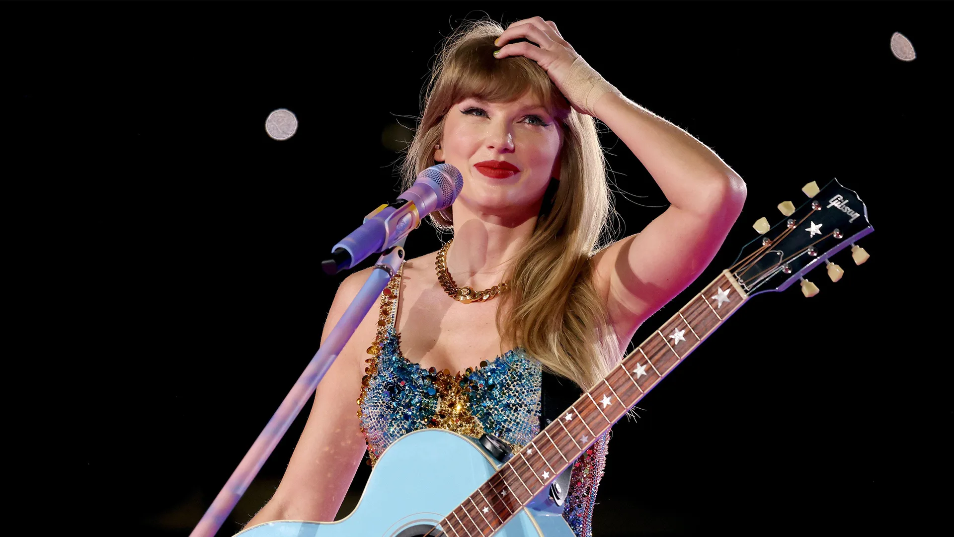 Taylor Swift smiling with blue guitar against a black background
