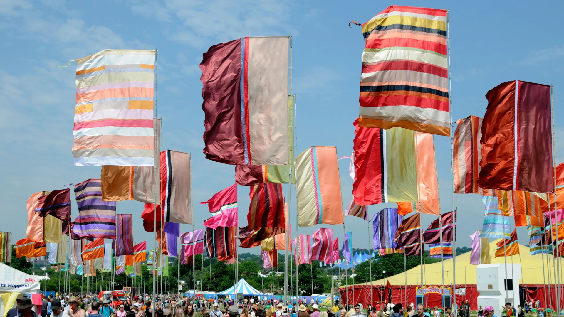 A photo of colourful festival flags against a blue sky with a crowd below