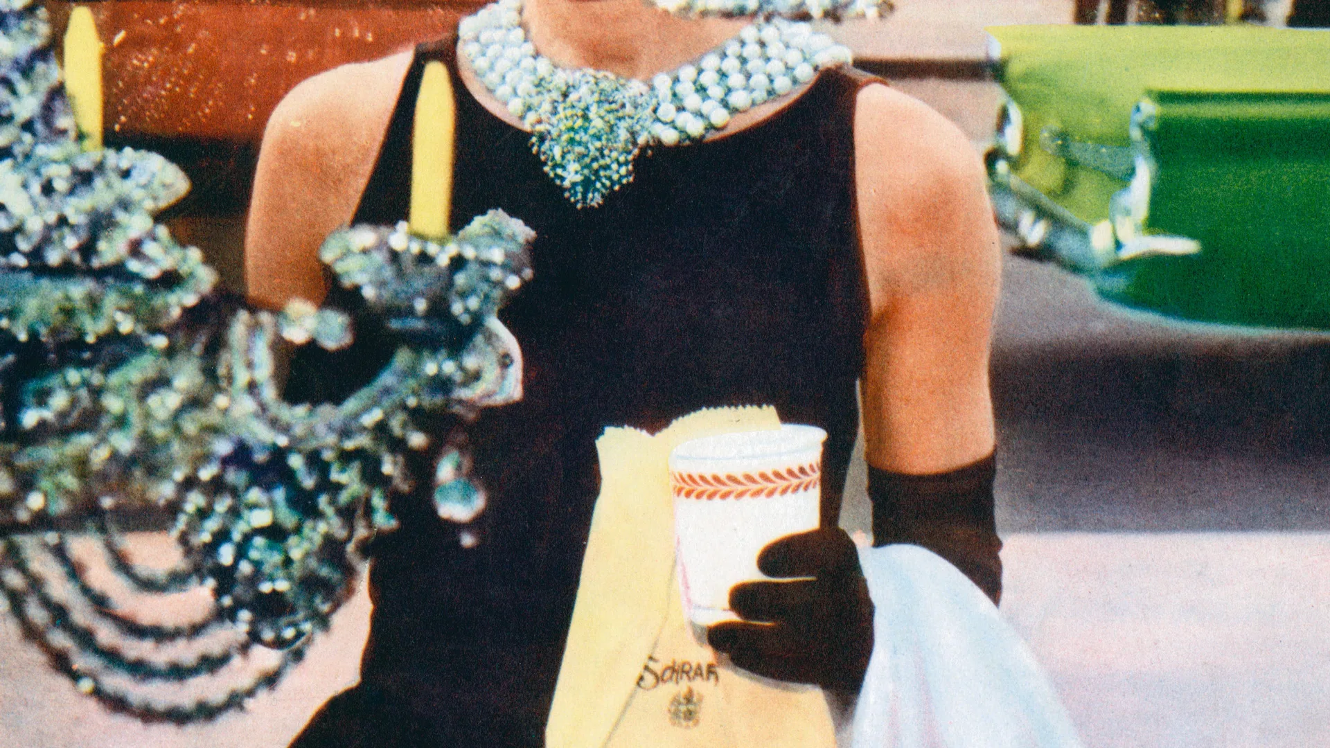 A photograph of a woman wearing a sparkly necklack and black dress holding a cup of coffee