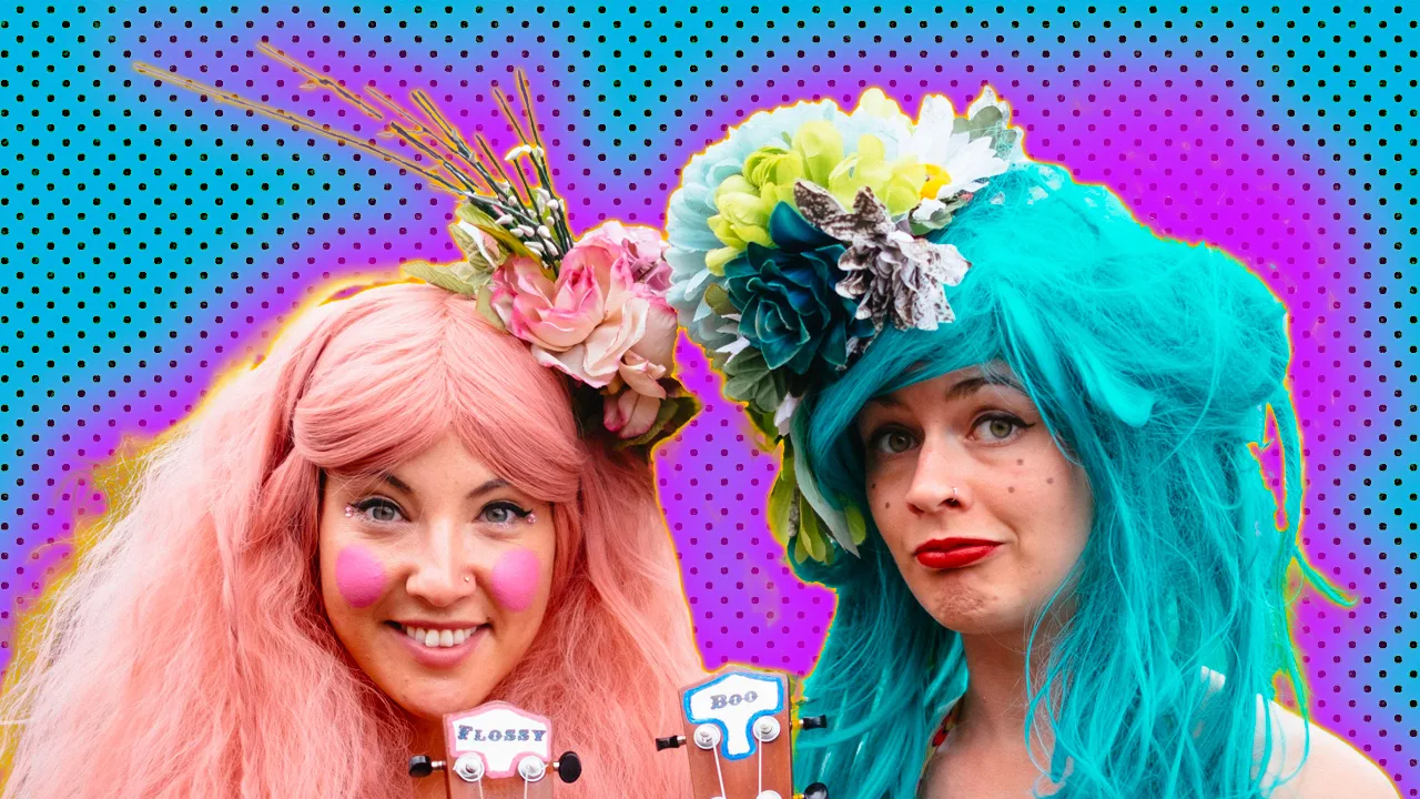 A photo of two women wearing bright colourful wigs and hair flowers against a blue dotted background with purple halo
