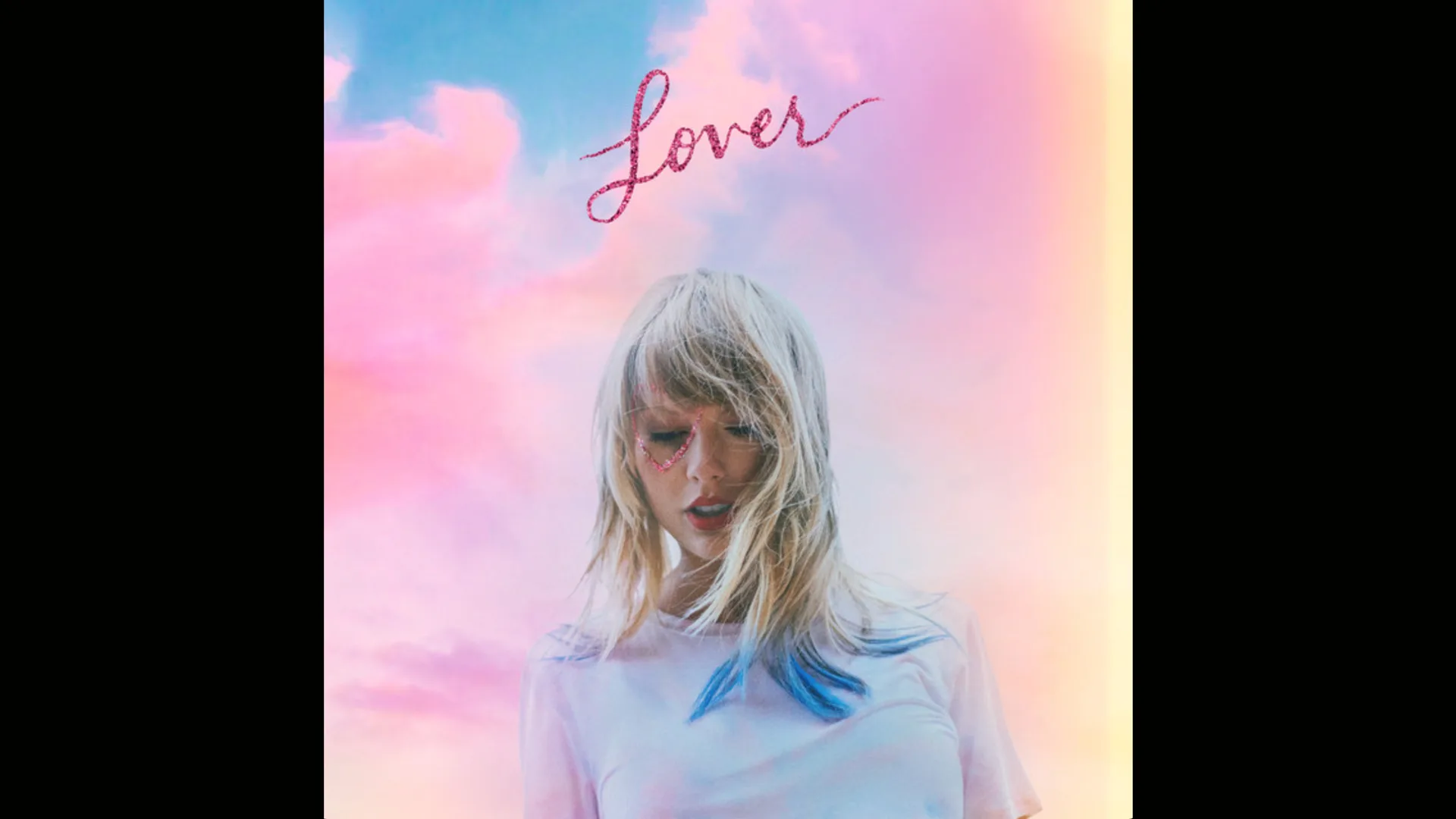 Taylor Swift's album LOVER showing the singing looking down with a red glitter heart drawn around her right eye and blue tips in her blonde hair. She is wearing a pastel coloured top and the words LOVER are above her in pink glitter against a pastel coloured cloudy sky or blues pinks and yellows.