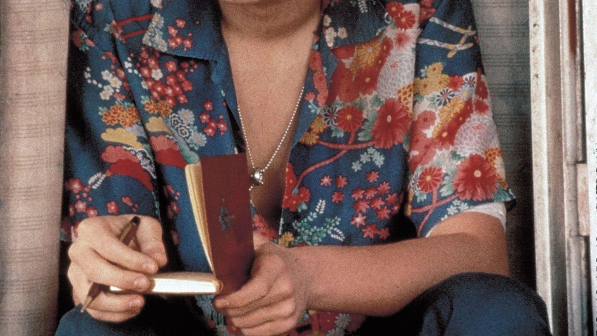 A photo of a man wearing a colourful hawaiian shirt holding a book and pen