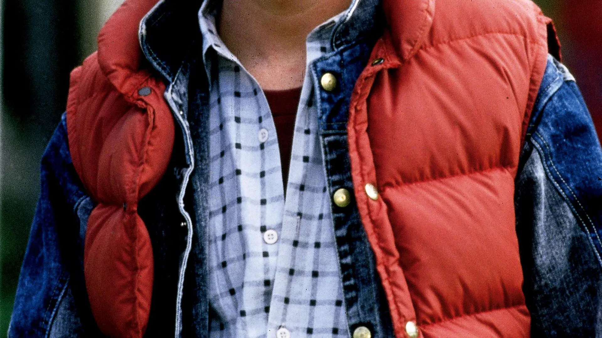 A photograph of a man wearing a red gilet and blue and grey plaid shirt
