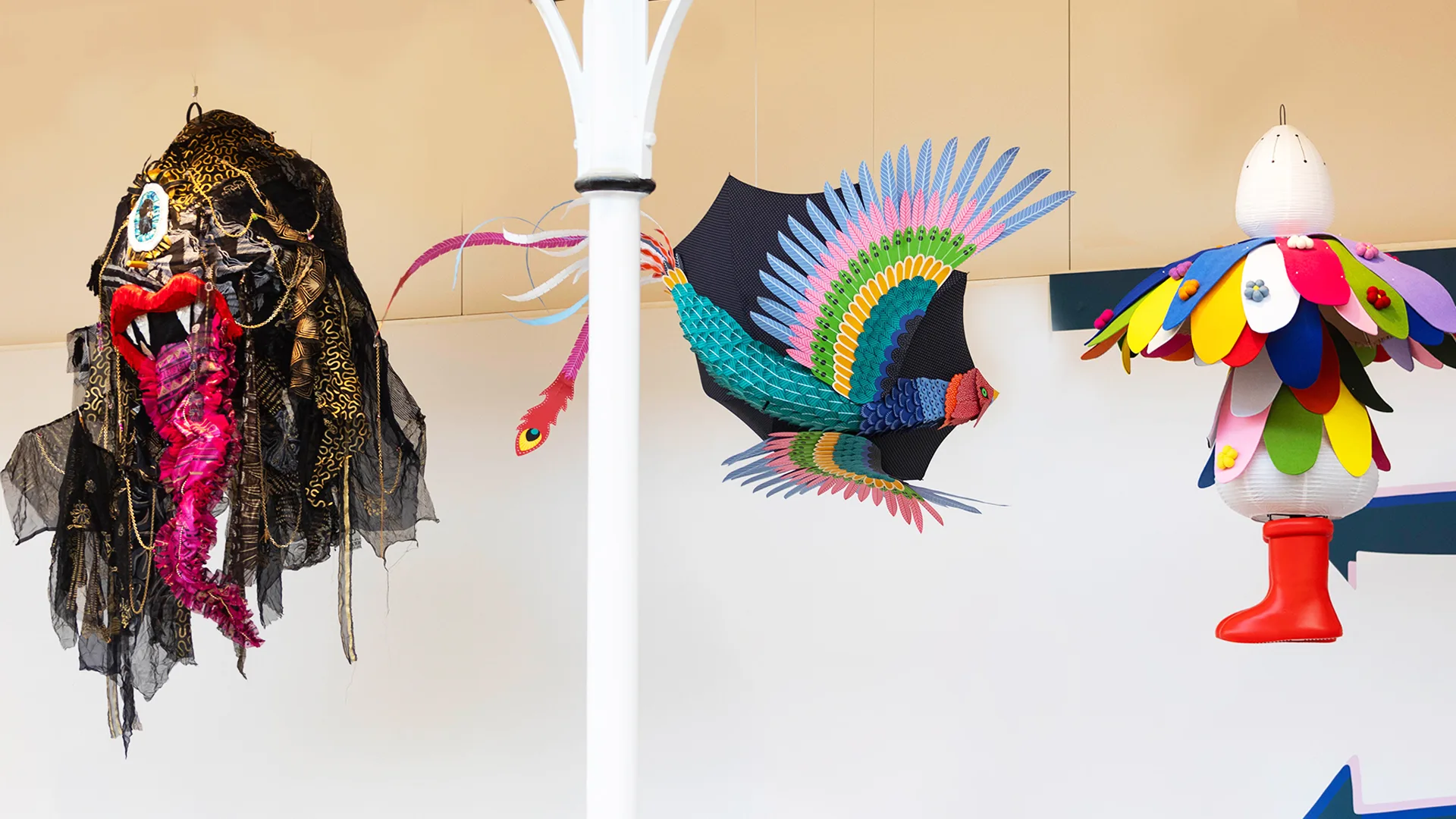 3 3d Yōkai hang from the ceiling at Young V&A museum, they are 3 Yōkai made from umbrellas. 1 is large and black with a big pink tongue, the second is a colourful bird, the third is one that looks like a human figure with a large flower for a head