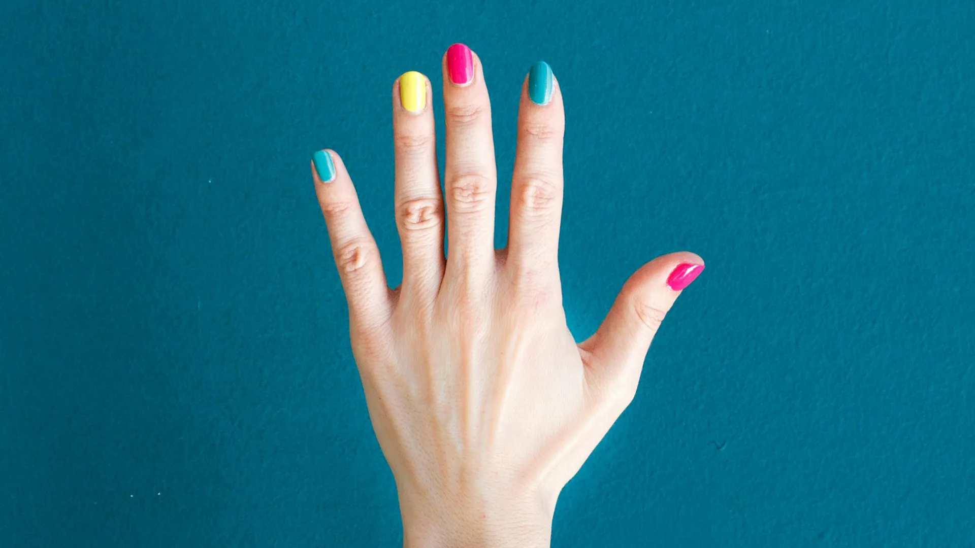 A hand with fingernails painted in blue, yellow and pink held out against a blue background