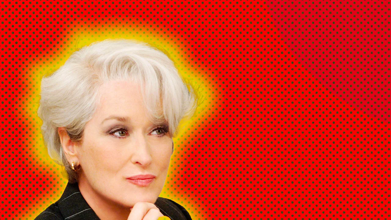 A photograph of Meryl Streep as the character Miranda Priestley in The Devil Wears Prada looking to the side with her hand to her face against a red dotted background with a yellow halo
