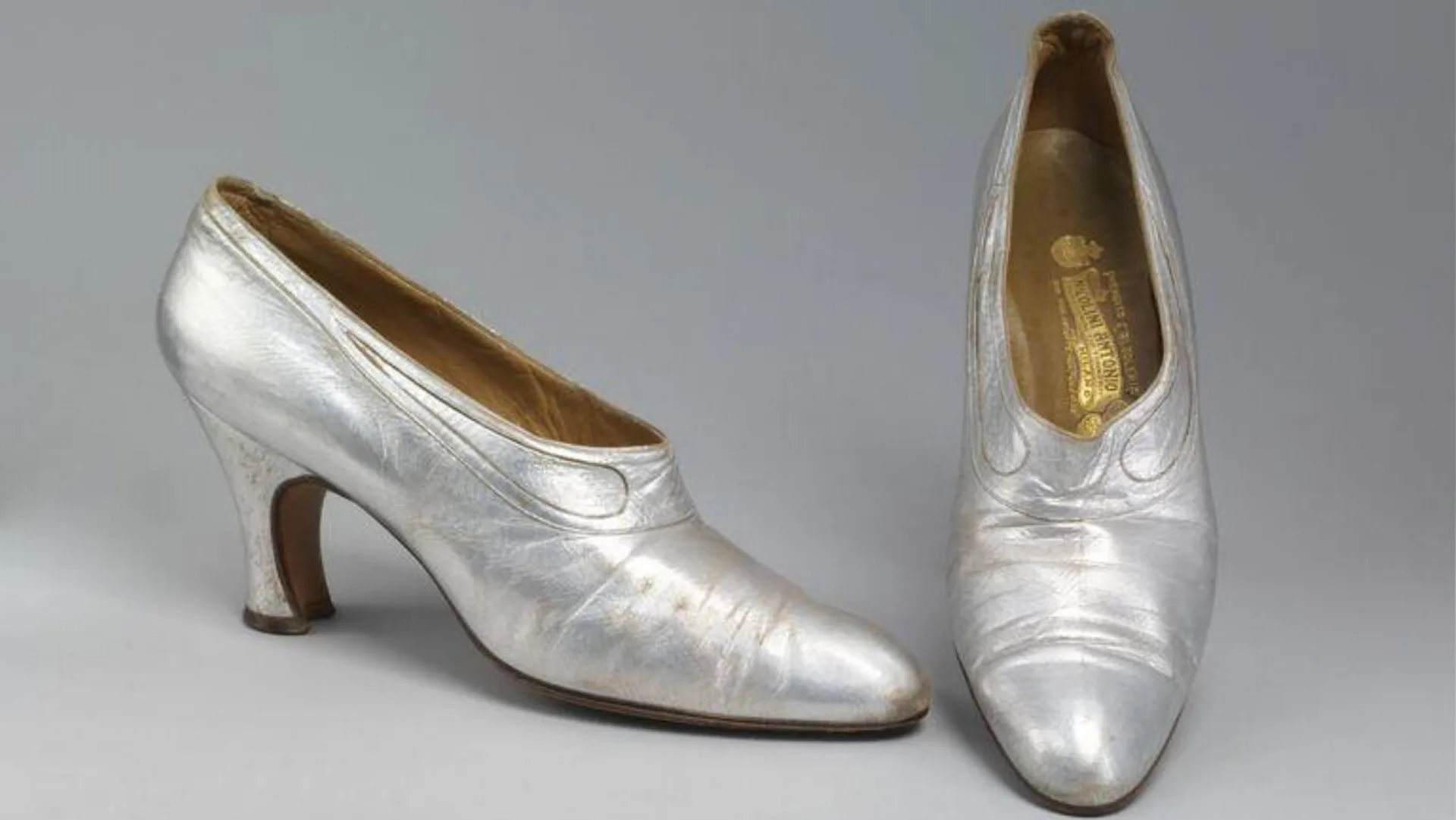 A photograph of a pair of silver dancing shoes against a grey background