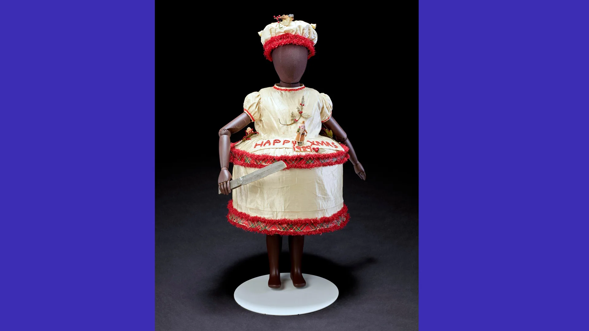 A photograph of a mannequin wearing a fancy dress christmas cake costume in white and red against a black background with blue borders