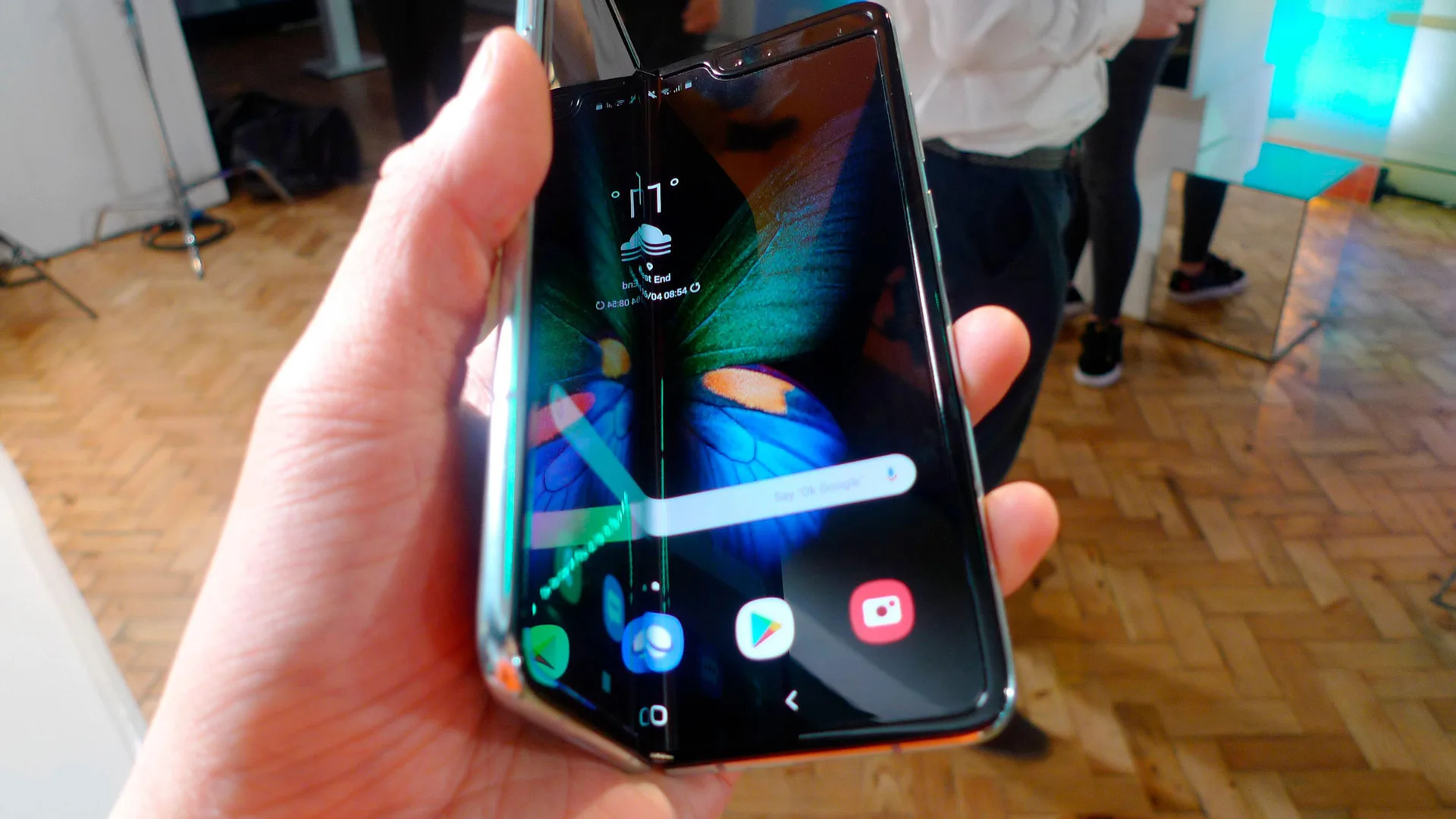 A photo of the galaxy samsung fold being held by a hand with the screen showing a partially folded butterly on LED