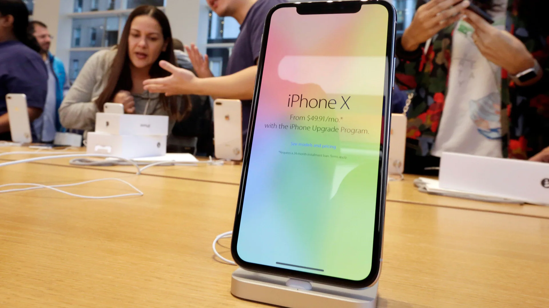 A photo of the iphone X in the apple store on a stand with the screen saying iPhone X and a rainbow background