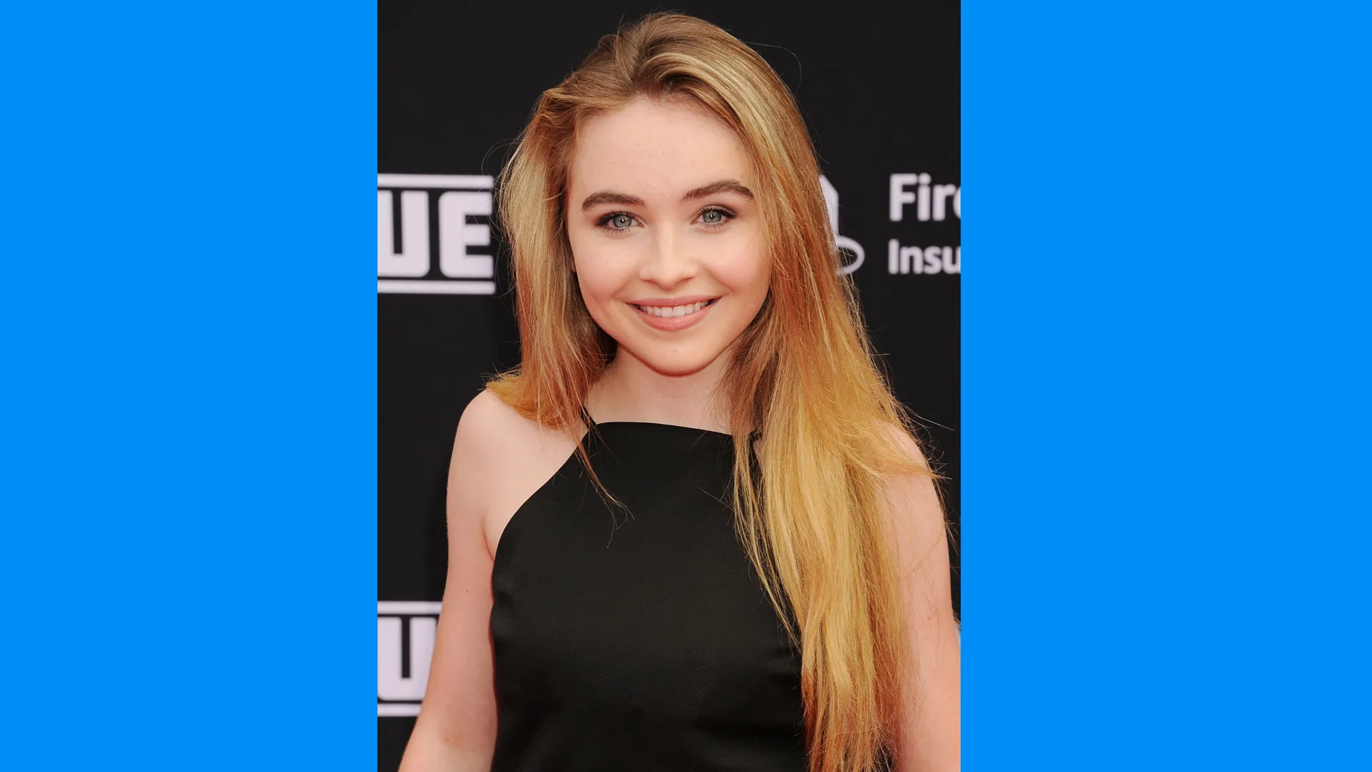 A photo of the singer actress Sabrina Carpenter smiling directly at the camera wearing a black top with blue borders either side