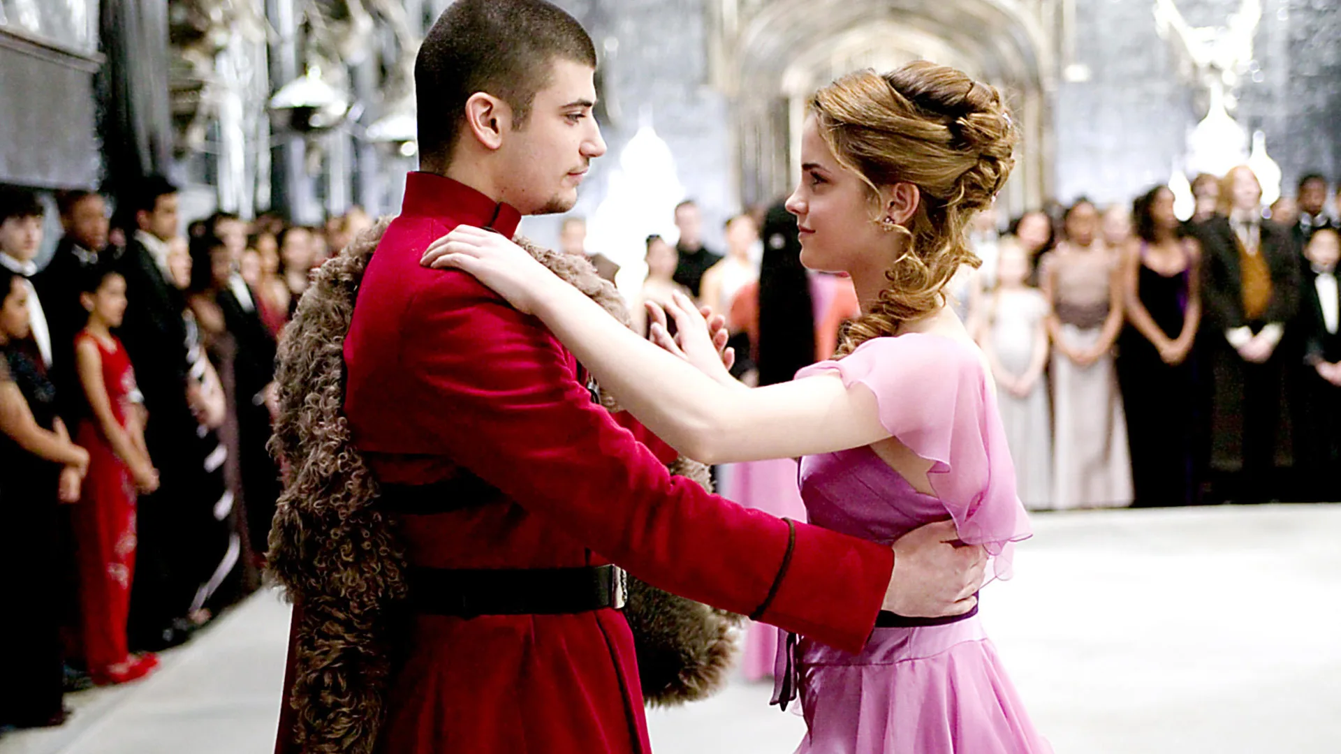 A still from Harry Potter and the Goblet of Fire showing Hermoine and her date dancing - she is wearing a pink dress and he a red suit