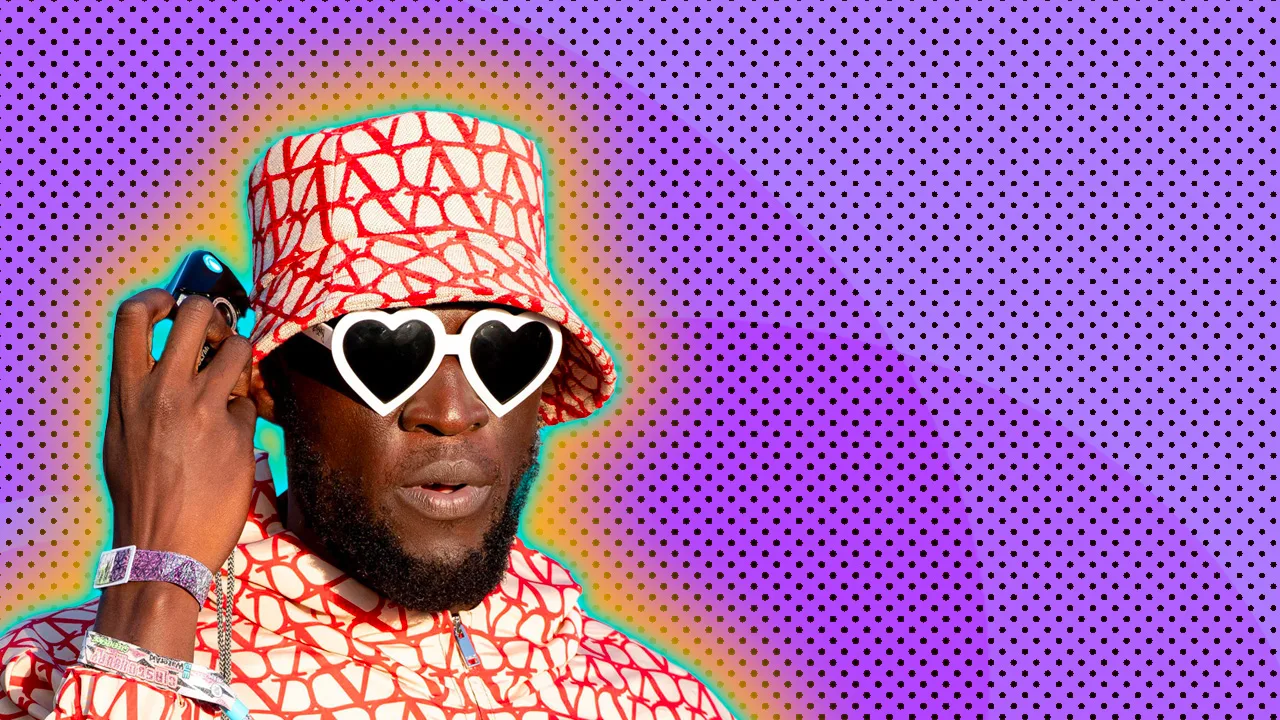 An image of Stormzy in a red and white Valentino hat and rainboat holding a phone up to his ear whilst wearing white heart shaped sunglasses against a purple dotted background with a green and orange halo.