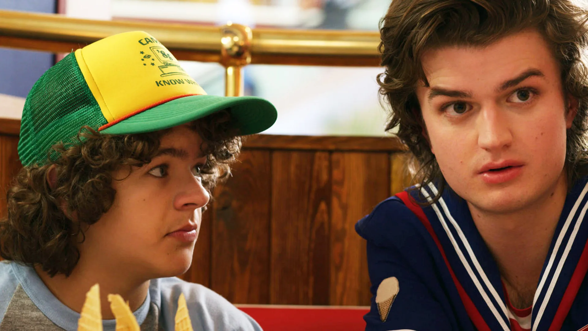 A photo of the characters Dustin and Steve from Stranger Things. Dustin is wearing his trademark trucker's hat in yellow and green and Steve is wearing his work outfit - a navy blue sailor suit.