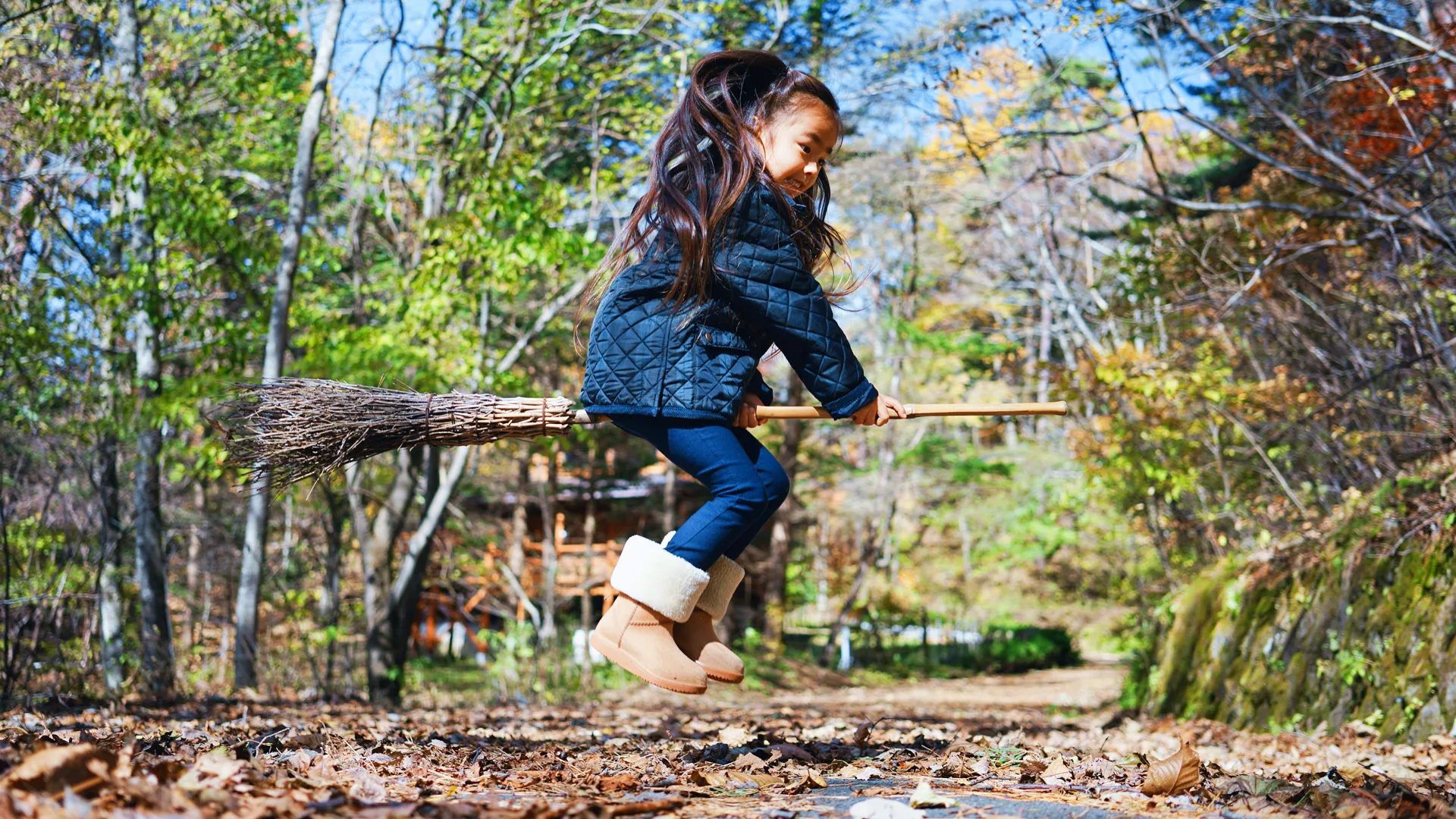 A photo of a little girl riding a broom stick in a forest